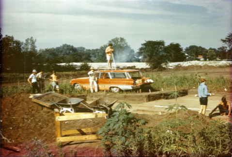 Dr. O'Brien atop the field vehicle with tripod for camera or mapping equipment (site location uknown, 1970s)