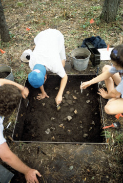 Students carefully brushing dirt from around a concentration of artifacts uncovered in their square 1x1 meter excavation unti at the Quarry Creek site (summer 1991)